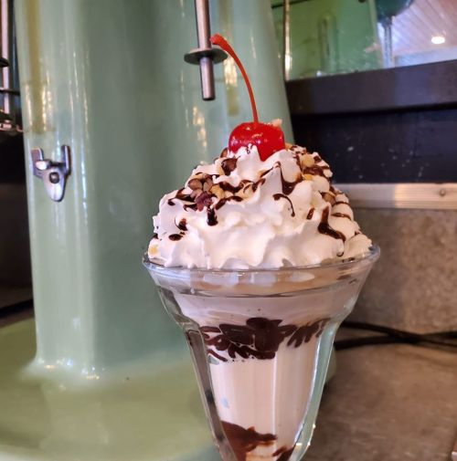 A delicious ice cream sundae topped with whipped cream, chocolate syrup, nuts, and a cherry, served in a glass dish.