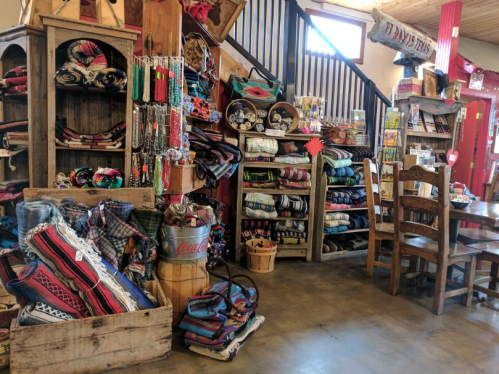 A cozy shop interior filled with colorful blankets, woven items, and handmade crafts, with wooden shelves and a table.