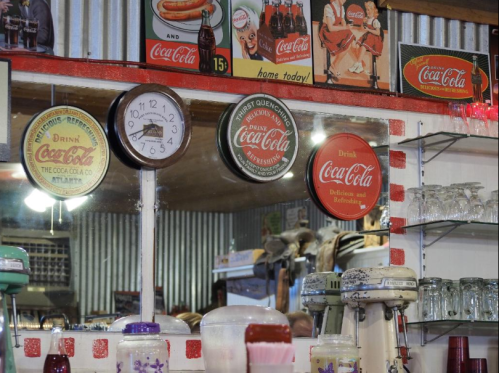 Vintage diner scene featuring Coca-Cola memorabilia, a clock, and retro glassware reflected in a mirror.