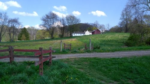 A scenic rural landscape featuring a white house, a red barn, and green fields under a blue sky with fluffy clouds.