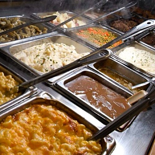 A buffet spread featuring various dishes, including macaroni and cheese, rice, vegetables, and gravy in metal trays.