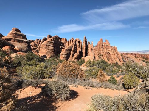Rocky formations rise against a clear blue sky, surrounded by sparse vegetation in a desert landscape.