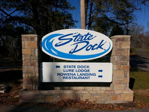 Sign for State Dock with directional arrows for Lure Lodge and Rowena Landing Restaurant, surrounded by trees.