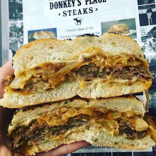 A hand holding a sliced sandwich filled with beef, onions, and cheese, with a menu in the background.