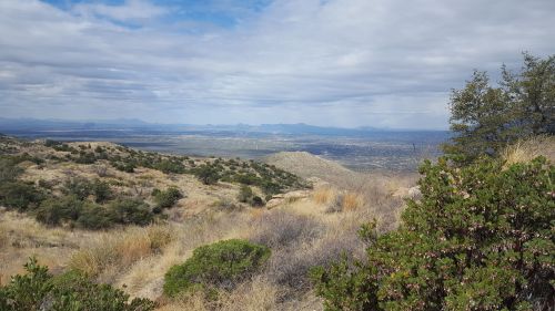 A panoramic view of a mountainous landscape with sparse vegetation and a cloudy sky in the background.