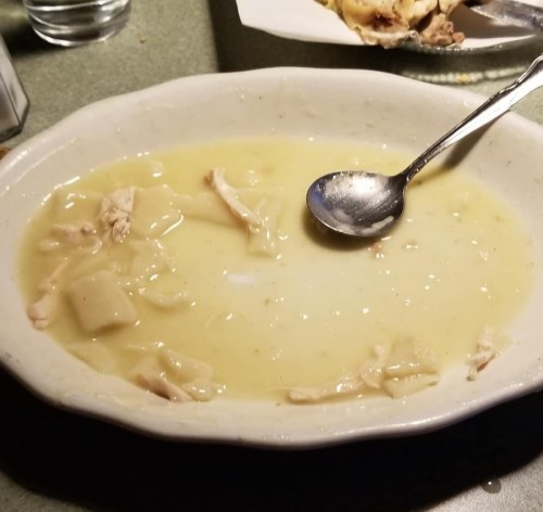 A shallow bowl with remnants of chicken and dumplings, featuring a spoon resting inside.
