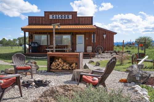 A rustic saloon-style building with a wooden porch, surrounded by a fire pit and outdoor seating in a grassy area.