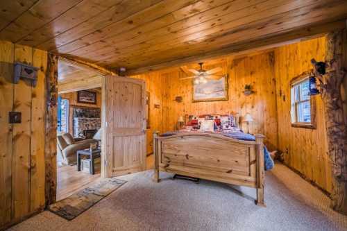 Cozy wooden bedroom with a bed, ceiling fan, and rustic decor, featuring warm tones and a welcoming atmosphere.