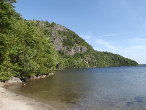 A serene lake bordered by lush green trees and a rocky hillside under a clear blue sky.