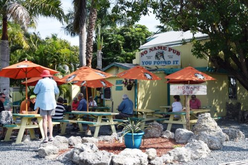 Outdoor dining area at No Name Pub, featuring colorful umbrellas, patrons, and tropical greenery.