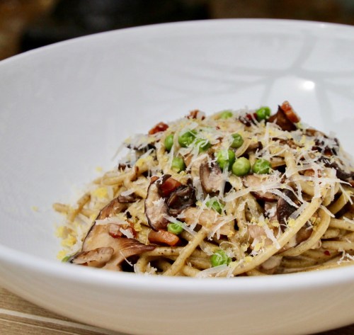 A bowl of pasta topped with mushrooms, green peas, and grated cheese, garnished with herbs.