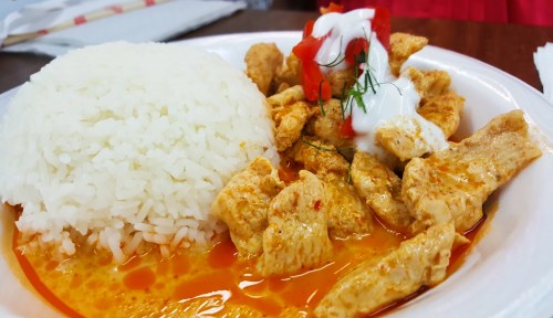 A plate of rice served with chicken in a creamy sauce, topped with diced tomatoes and a dollop of sour cream.