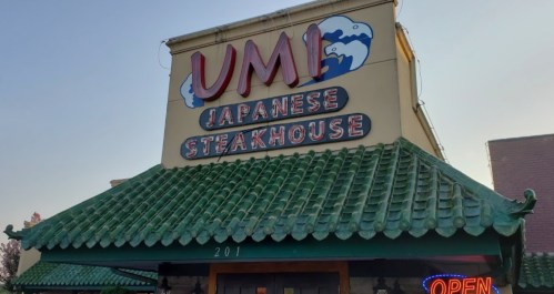 Exterior of UMI Japanese Steakhouse with a green tiled roof and a bright "OPEN" sign.