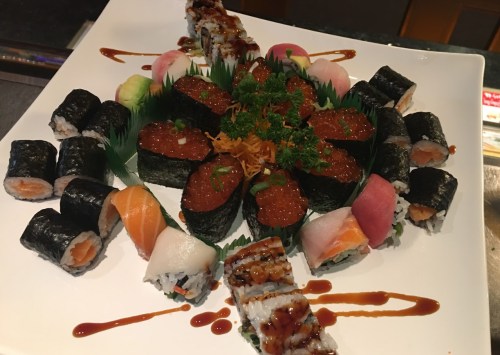 A beautifully arranged platter of various sushi rolls, including nigiri, maki, and garnishes, on a white plate.