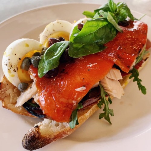 A toasted bread slice topped with smoked salmon, hard-boiled eggs, olives, capers, and fresh greens.