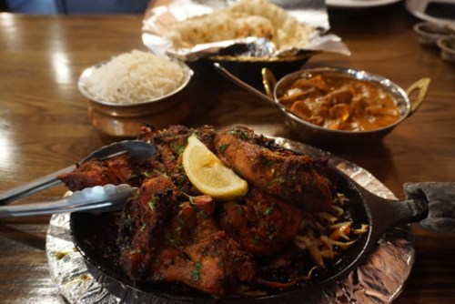 A sizzling platter of grilled chicken with lemon, served alongside rice, naan, and a bowl of curry.