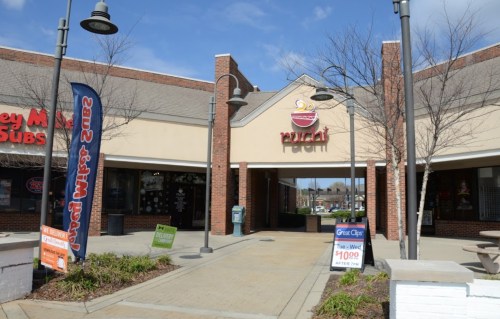 Entrance to a shopping plaza featuring signs for various businesses, including a sandwich shop and a hair salon.