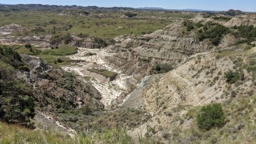 A vast landscape featuring rugged hills, valleys, and greenery under a clear blue sky.