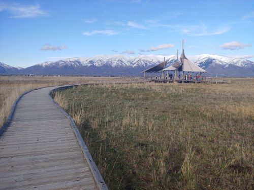 A wooden walkway leads to a pavilion with mountains in the background under a clear blue sky.