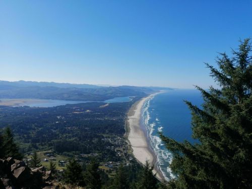 A panoramic view of a coastline with sandy beaches, waves, and mountains under a clear blue sky.