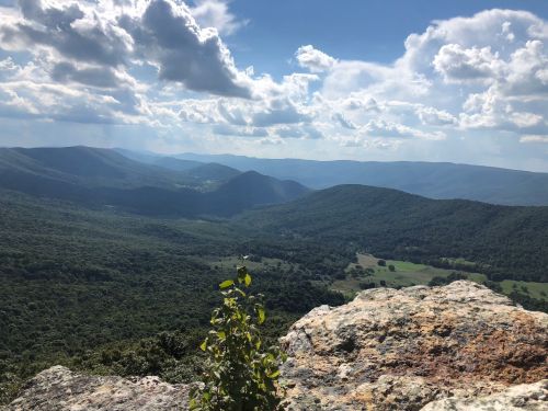 A panoramic view of rolling green mountains under a partly cloudy sky, with a rocky foreground.
