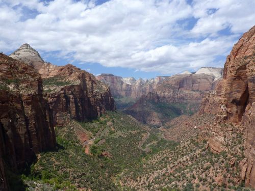 A panoramic view of Zion National Park, showcasing red rock formations and lush greenery under a partly cloudy sky.