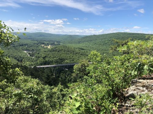 A scenic view of lush green mountains and a highway bridge under a blue sky with scattered clouds.