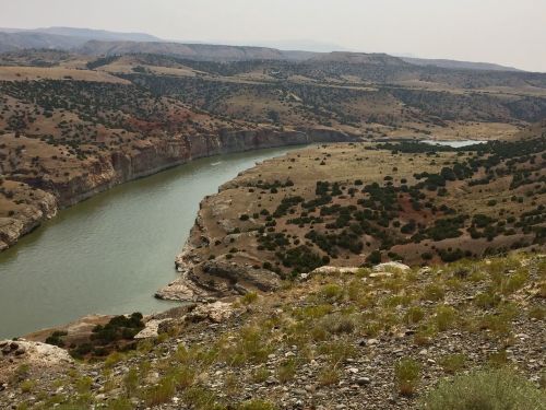 A winding river flows through a rugged landscape of hills and sparse vegetation under a hazy sky.