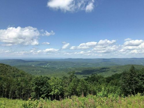 A panoramic view of lush green mountains under a blue sky with fluffy white clouds.
