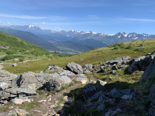 A scenic view of mountains and valleys, with rocky terrain and lush greenery under a clear blue sky.