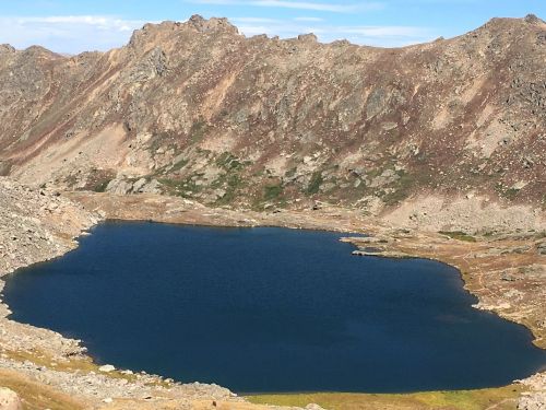 A serene mountain lake surrounded by rocky terrain and peaks under a clear blue sky.