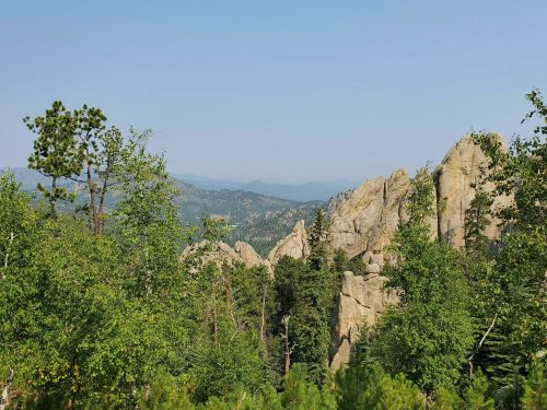 A scenic view of rocky mountains surrounded by lush green trees under a clear blue sky.