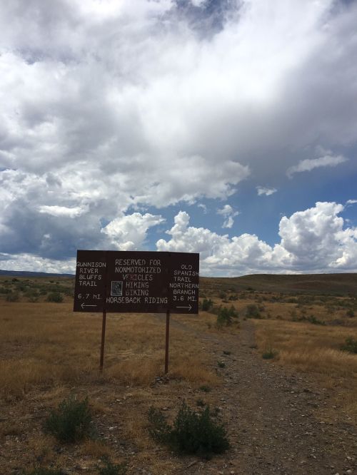 Signpost indicating trail options for hiking and horseback riding, set against a cloudy sky and grassy landscape.