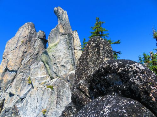 A rocky landscape with towering granite formations against a clear blue sky and scattered evergreen trees.