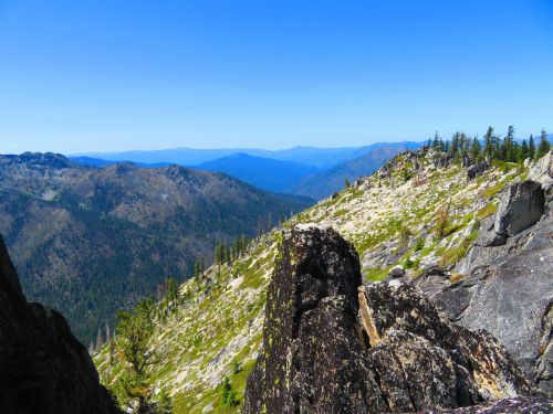 A panoramic view of rugged mountains and lush greenery under a clear blue sky.