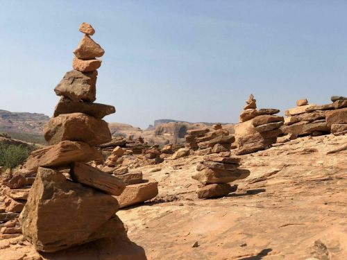 A stack of rocks balanced on a rocky landscape under a clear blue sky, with more rock formations in the background.
