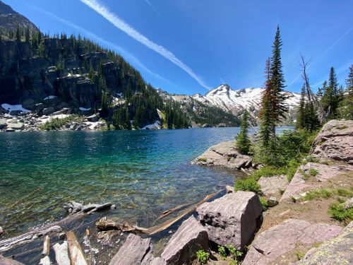 A serene lake surrounded by mountains, with clear blue water and lush greenery under a bright blue sky.