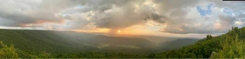 A panoramic view of a lush green valley at sunset, with dramatic clouds and a warm glow on the horizon.