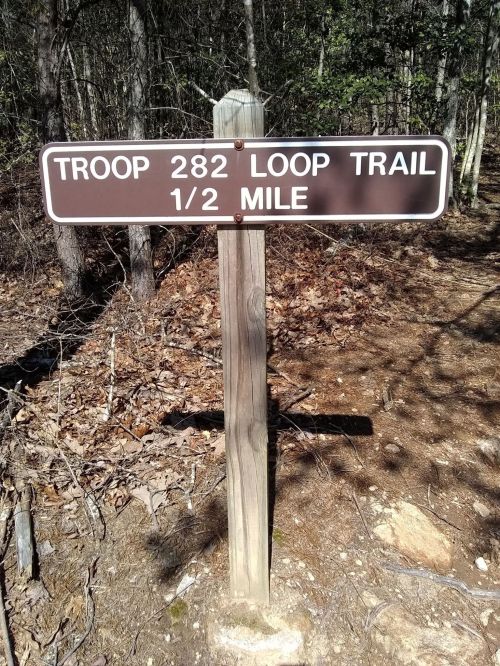 Sign for Troop 282 Loop Trail, indicating a distance of 1/2 mile, set in a wooded area.