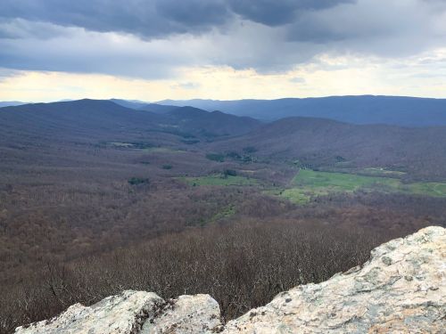 A panoramic view of rolling mountains and valleys under a cloudy sky, with patches of green and brown foliage.
