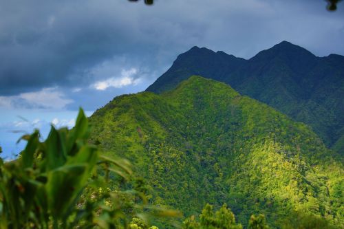 Lush green mountains under a cloudy sky, showcasing vibrant vegetation and dramatic peaks.