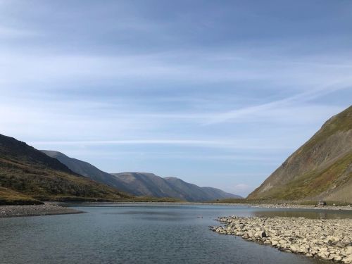 A serene landscape featuring a calm river surrounded by mountains under a clear blue sky.