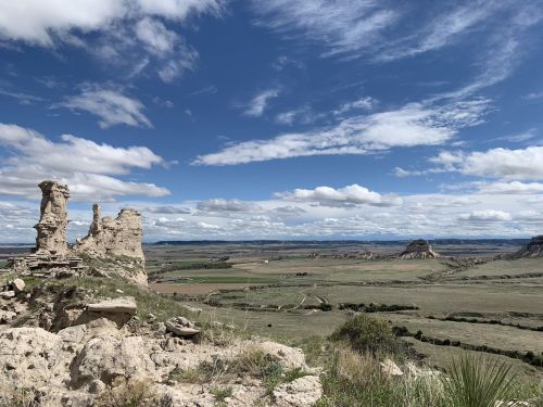A vast landscape featuring rocky formations, rolling hills, and a blue sky with scattered clouds.