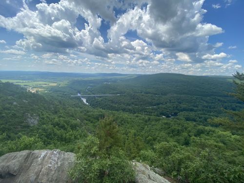 A panoramic view of lush green mountains and a river under a bright, cloudy sky.