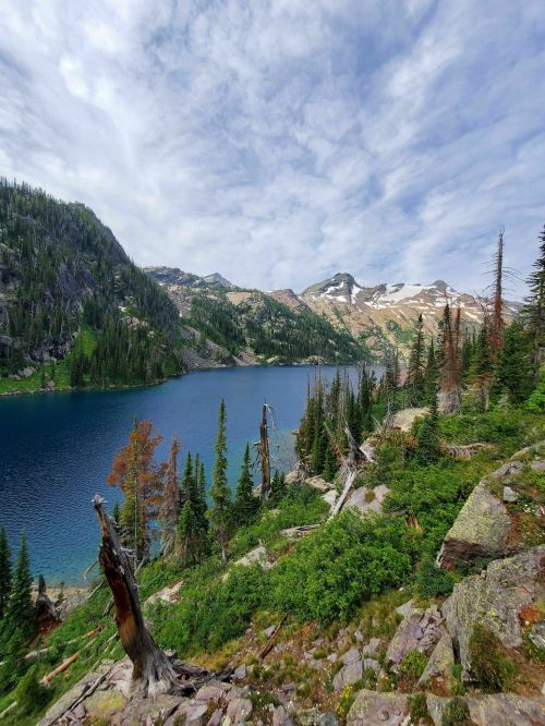 A serene mountain lake surrounded by lush greenery and rocky terrain under a partly cloudy sky.