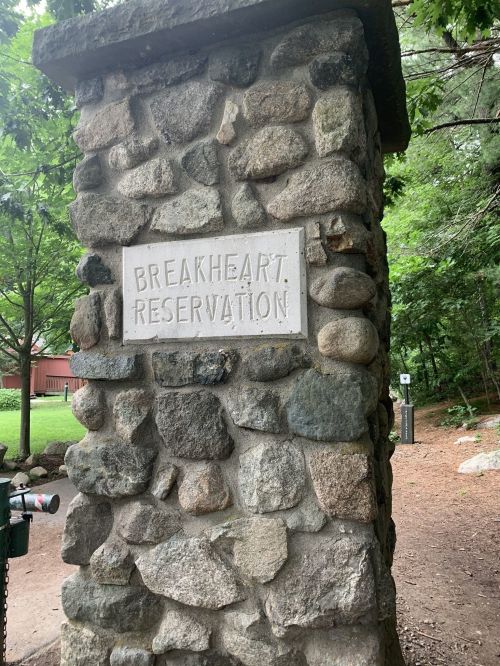 Stone pillar with a sign reading "Breakheart Reservation" surrounded by trees and greenery.