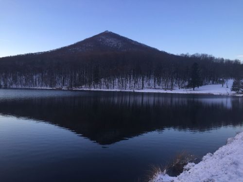 A serene winter landscape featuring a snow-covered mountain reflected in a calm lake.