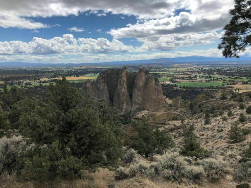 A scenic view of rocky cliffs surrounded by green fields and trees under a partly cloudy sky.