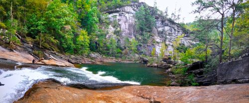 A serene landscape featuring a river flowing over rocks, surrounded by lush greenery and steep cliffs.