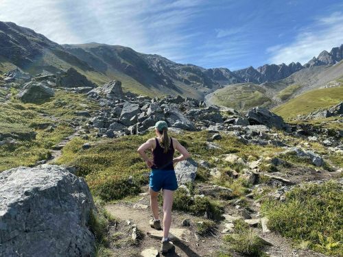 A person hiking on a rocky trail in a mountainous landscape under a clear blue sky.